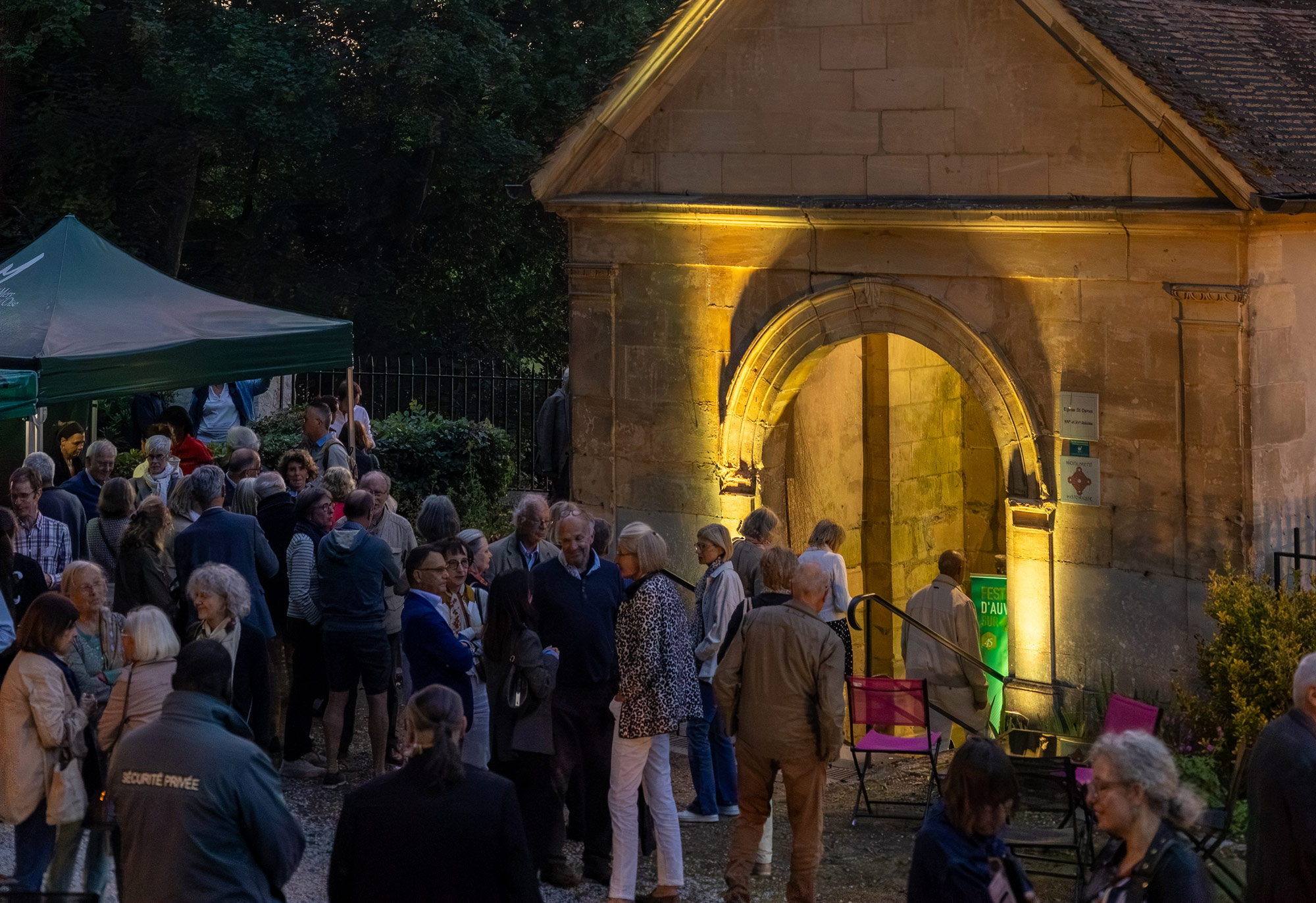 Audience of the Festival d'Auvers-sur-Oise outside the illuminated Saint-Denis church on a concert evening